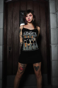 Woman wearing a black tank top with a graphic design in a dimly lit room.