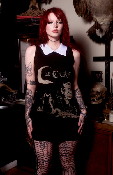 Person wearing a black sleeveless top with graphic design in a dark, possibly gothic-themed room.