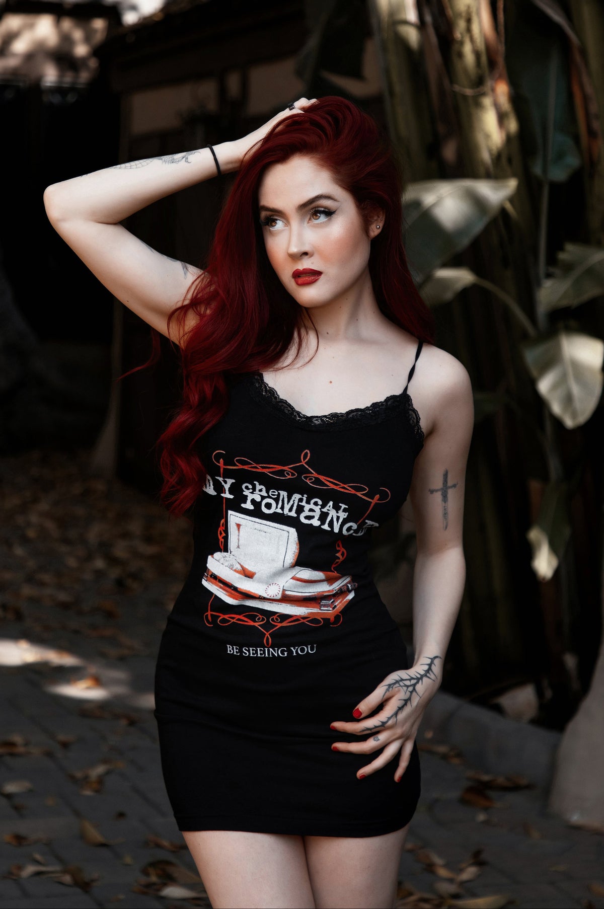 Woman with red hair wearing a black tank top with graphic design outdoors.