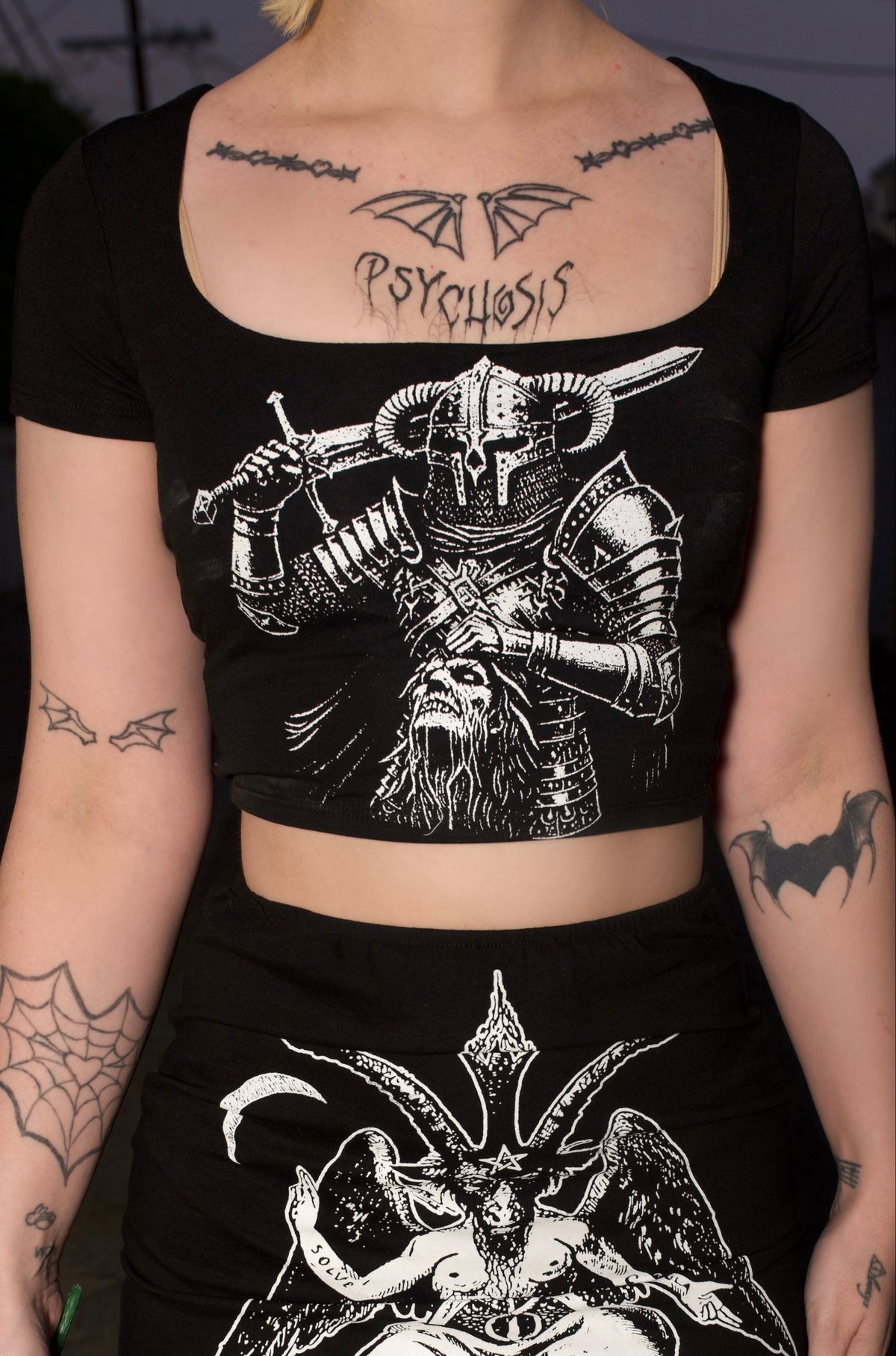 Person wearing a black outfit with graphic designs, holding red roses in a dark setting.