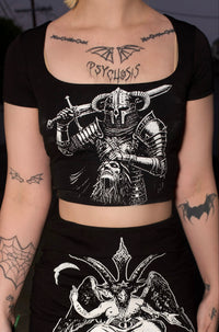 Person wearing a black outfit with graphic designs, holding red roses in a dark setting.
