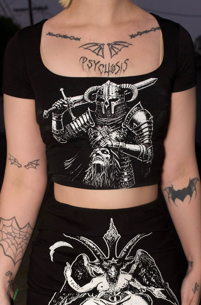 Person wearing a black outfit with graphic designs, holding red roses in a dark setting.