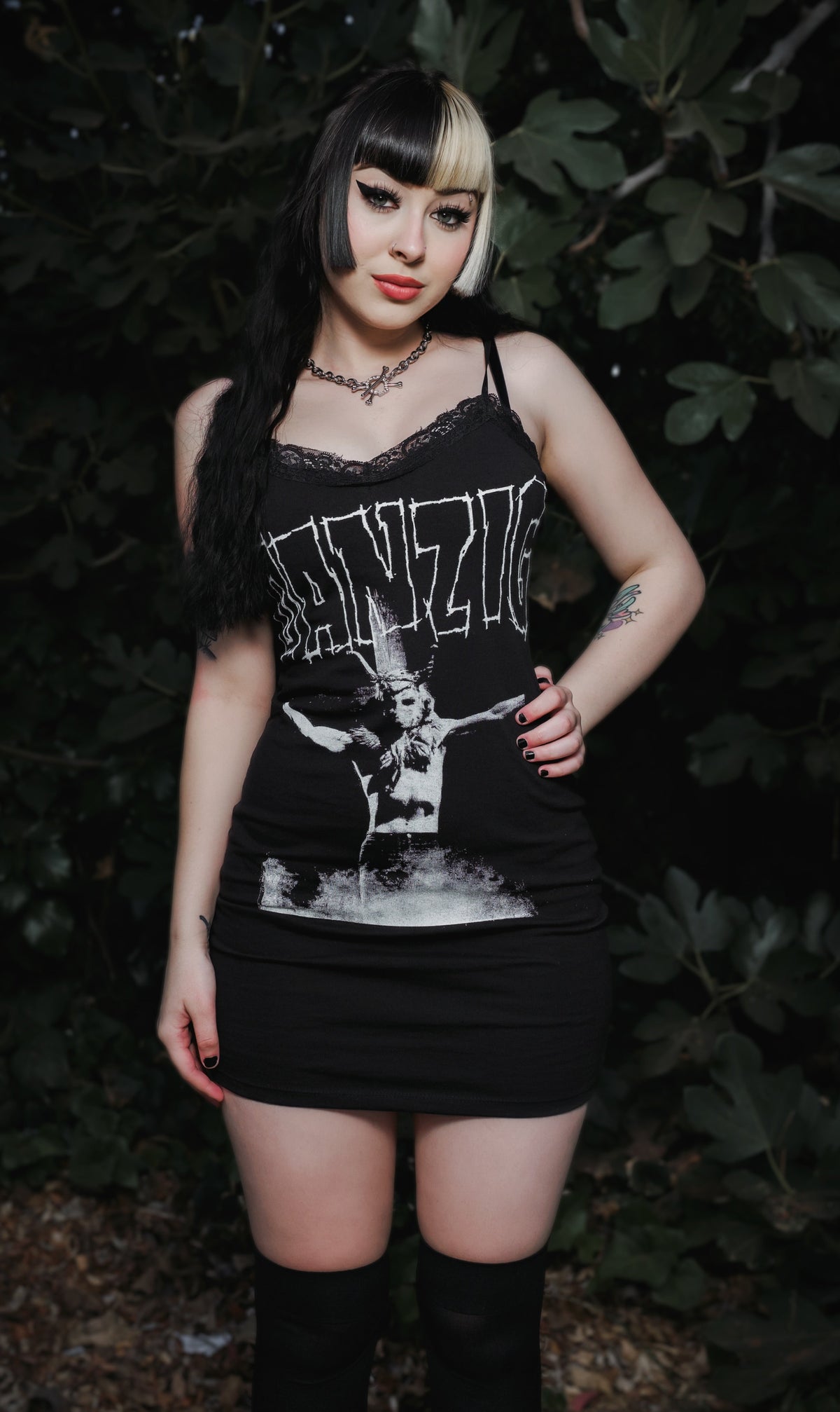 Person wearing a black tank top with graphic design and text, standing against a dark background.