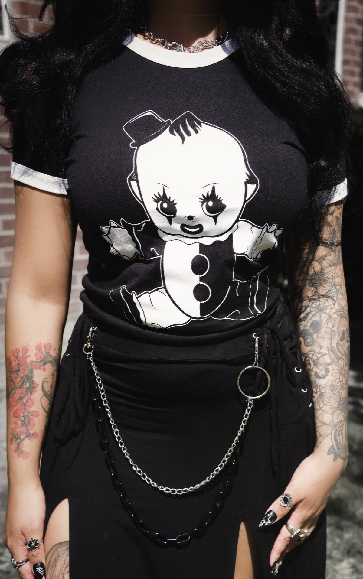 Person wearing a black t-shirt with a graphic design and a black skirt with chains, standing outdoors.
