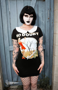 Person wearing a black dress with a graphic design and 'No Doubt' text, standing against a wooden gate.