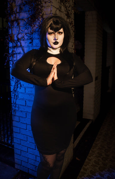 Person in a black dress with blue lighting against a brick wall.