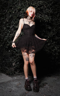Person wearing a black dress with sheer overlay against a dark background