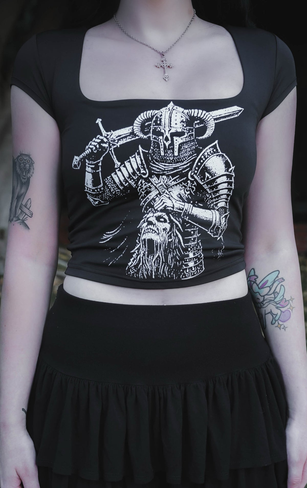 Person wearing a black top with a white graphic design and a black skirt outdoors.