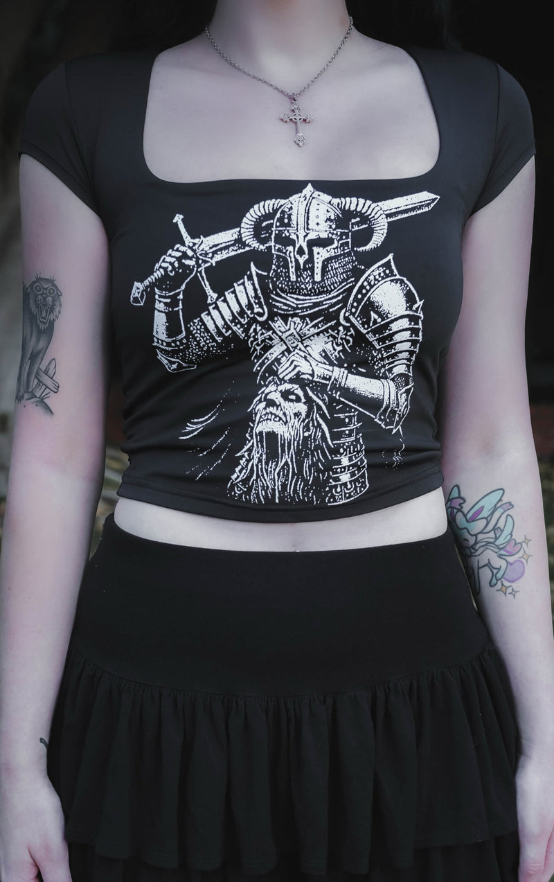 Person wearing a black top with a white graphic design and a black skirt outdoors.