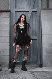 Woman in black outfit with lace details standing in front of a wooden door.