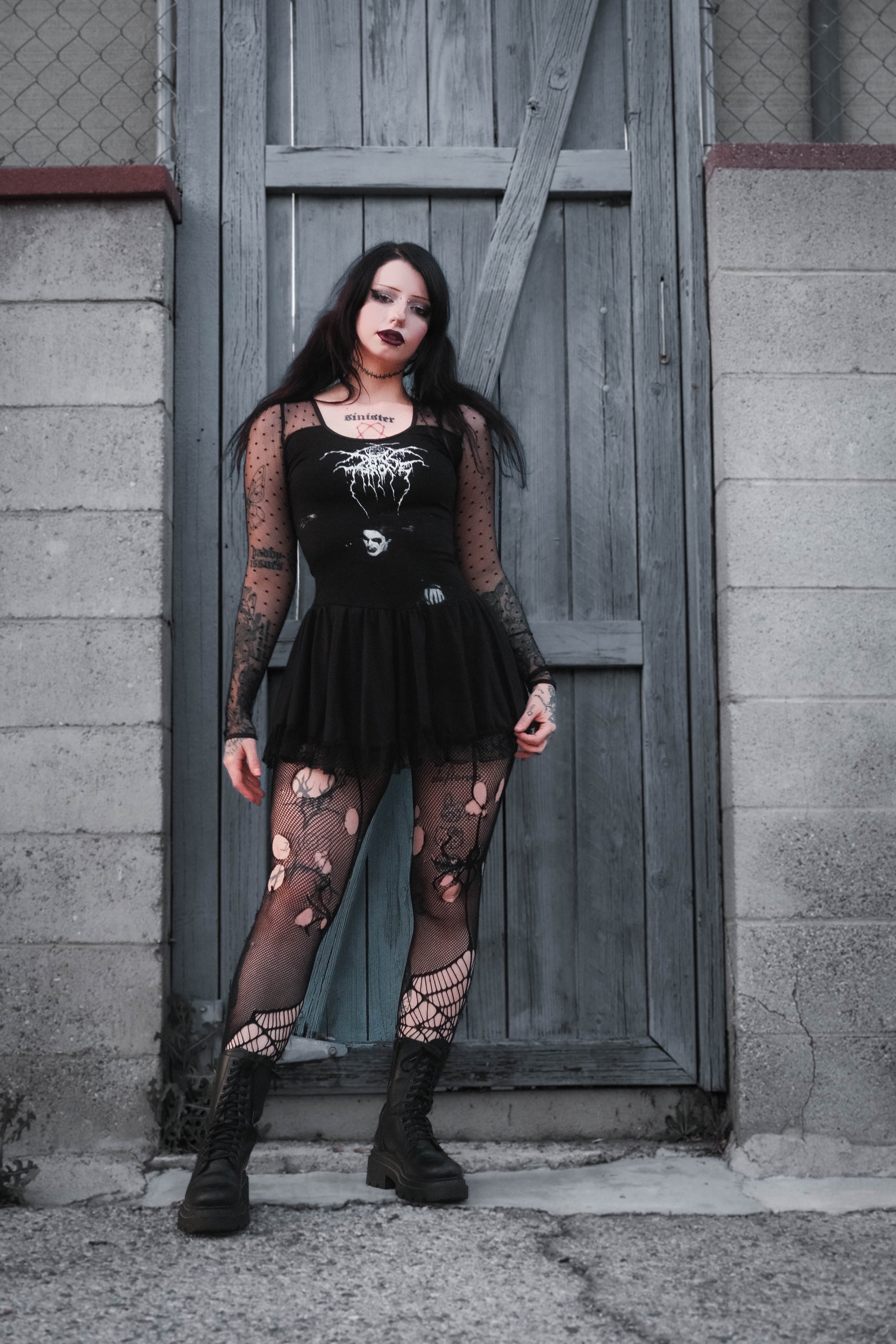 Woman in black outfit with lace details standing in front of a wooden door.