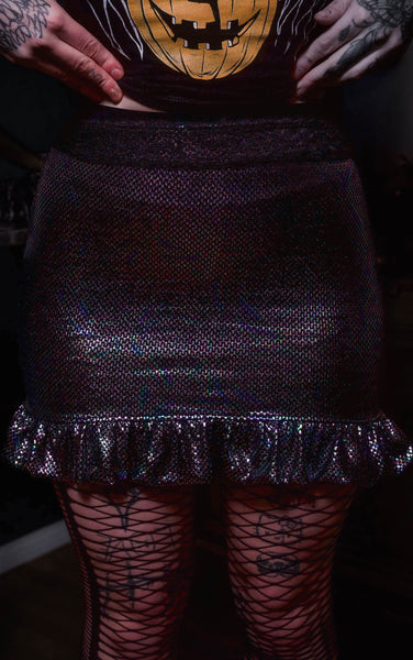 Person wearing a dark purple glittery skirt with fishnet stockings and tattooed hands.