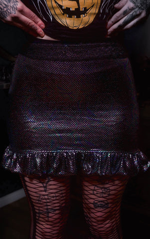 Person wearing a dark purple glittery skirt with fishnet stockings and tattooed hands.