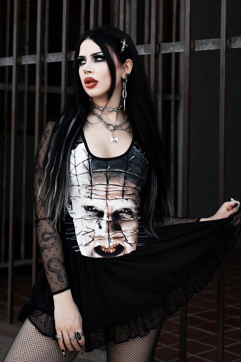 Woman wearing a black dress with a graphic design, standing in front of a metal gate.