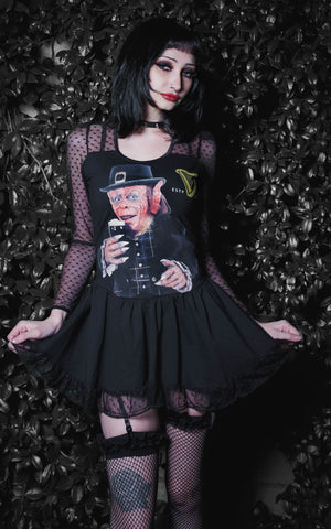 Person wearing a black dress with a graphic design, standing against a dark leafy background