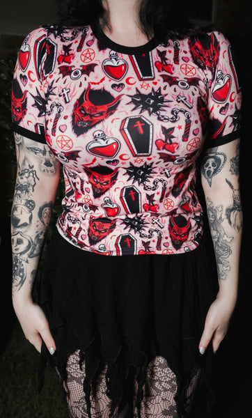 Person wearing a black and red patterned top with tattoos on arms