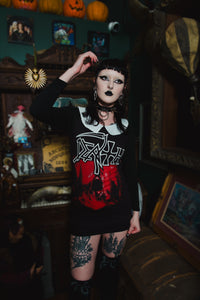Person wearing a black dress with a graphic design in a dark, decoratively adorned room.