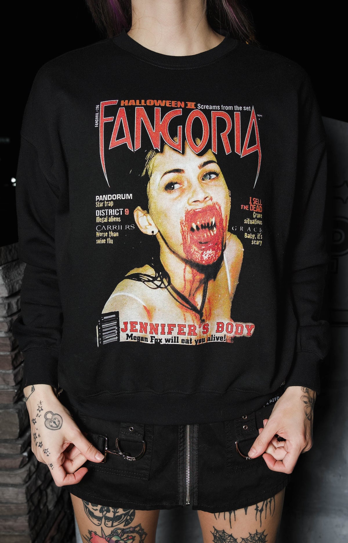 Person wearing a black sweatshirt with a graphic design and text, standing against a dark background.