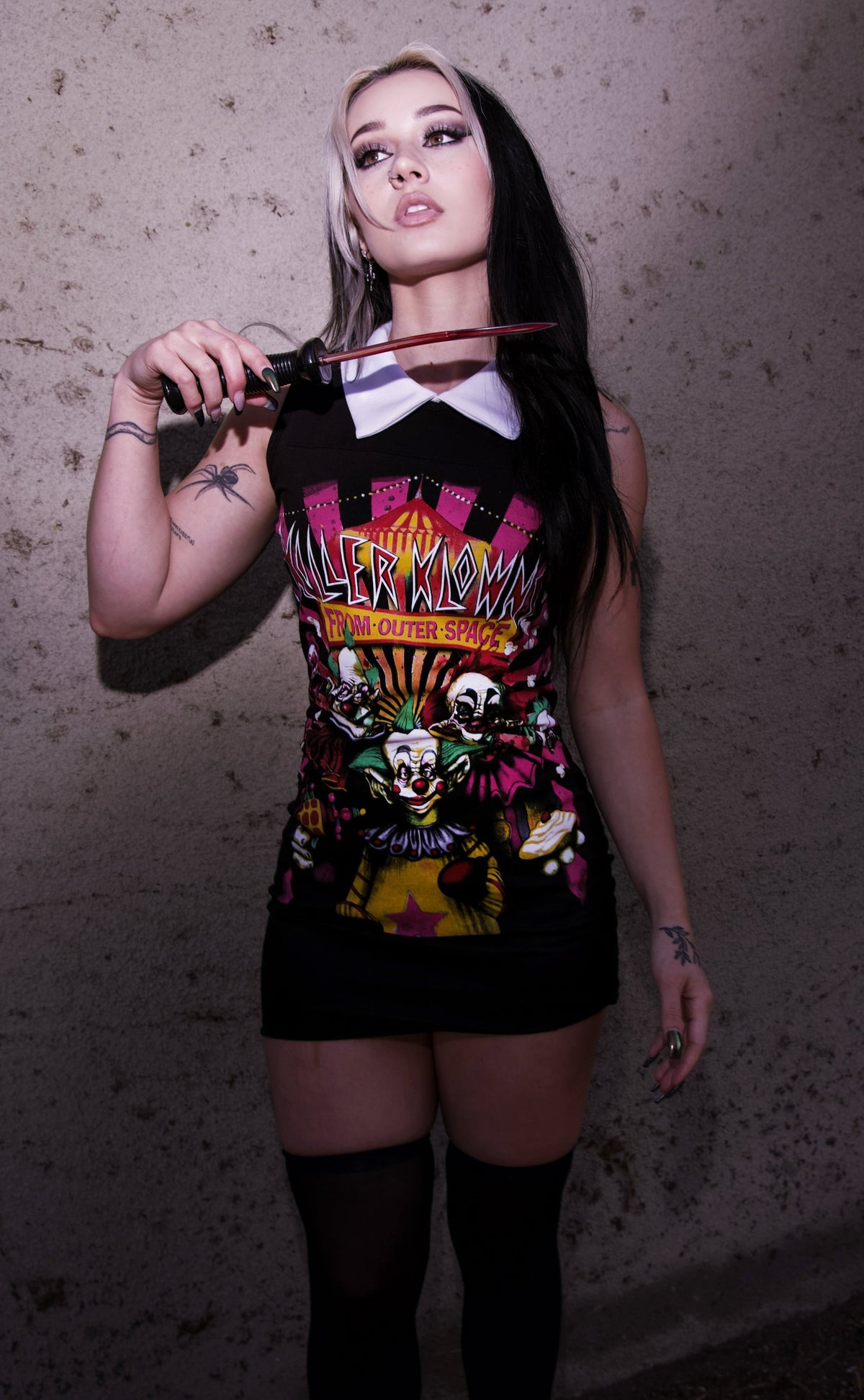 Person wearing a colorful tank top with graphic design against a textured wall.