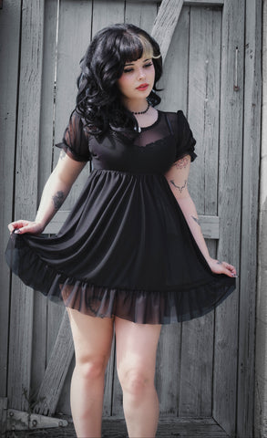 Woman wearing a black dress standing against a wooden wall.