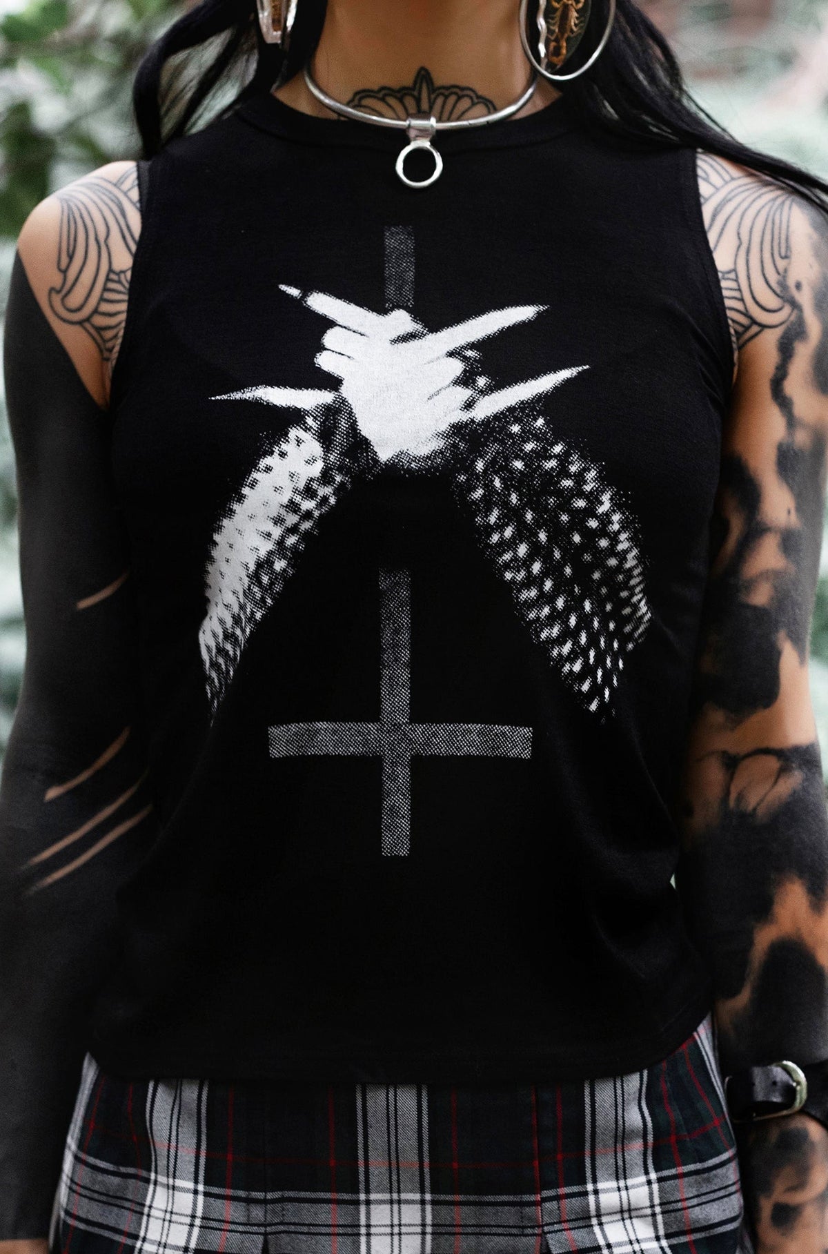 Person wearing a black sleeveless top with a graphic design and a plaid skirt.