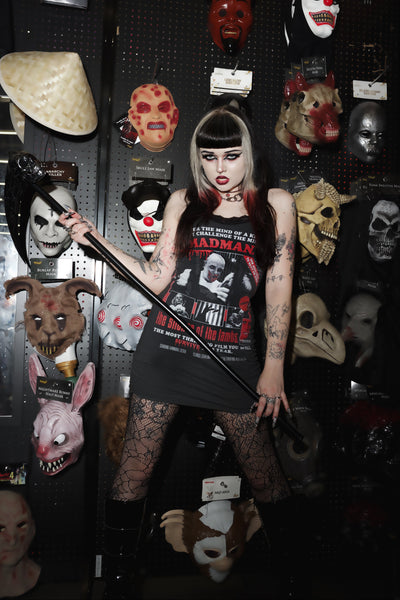 Person wearing a 'Badman' t-shirt surrounded by various masks on a pegboard.