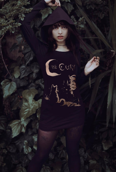 Person wearing a dark hoodie with a graphic design in a natural setting