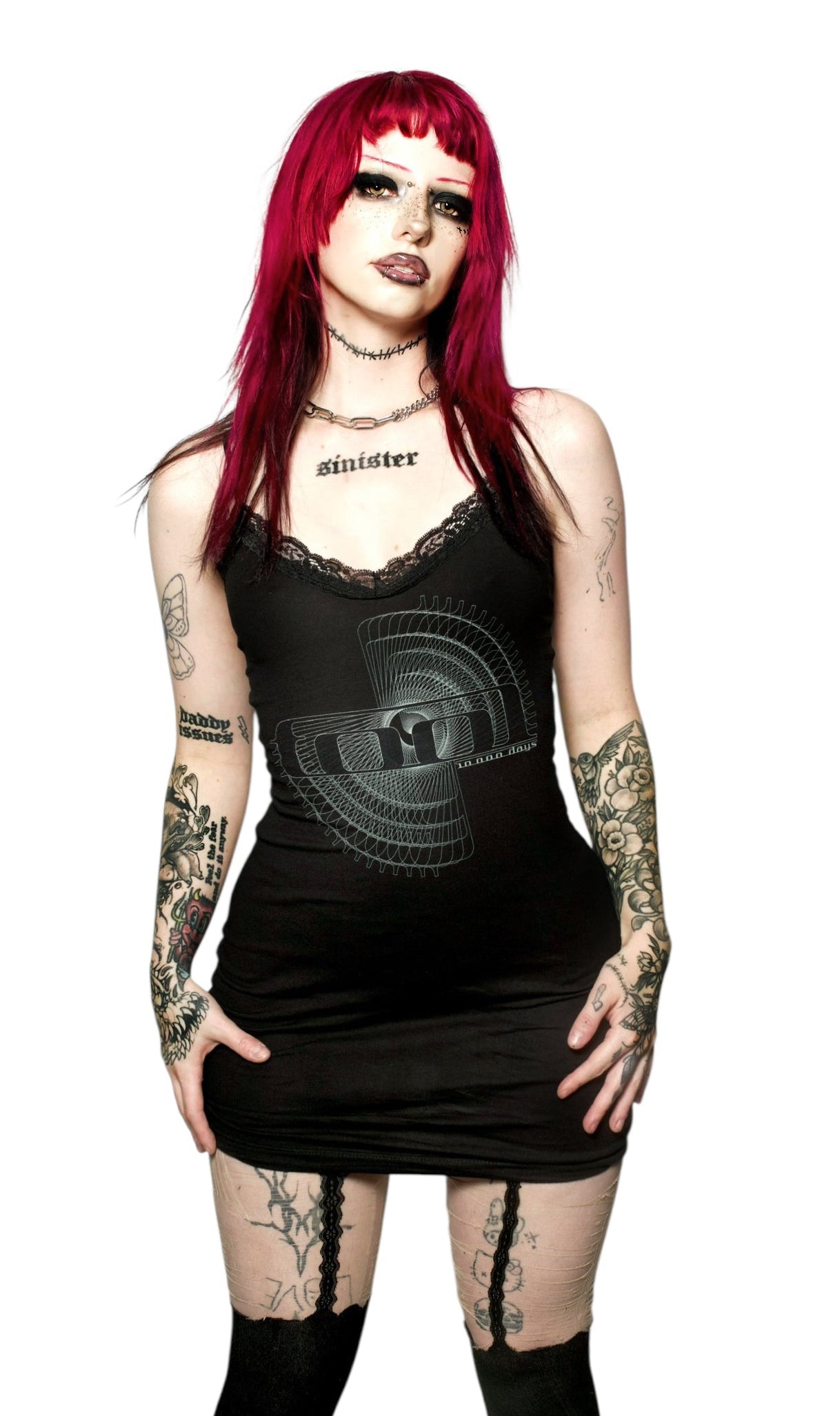 Woman with red hair and tattoos wearing a black dress with geometric design on a white background