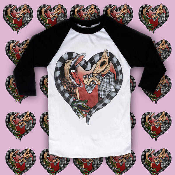 White baseball tee with black sleeves and black neckline trim. Features image of Barbara and Adam from the movie Beetlejuice. Barbara has face stretched with mouth open, tongue sticking out and eyes in mouth. Adam has his face stretched out with eyeballs on his fingers and glasses in hand. Black and white Beetlejuice snake around Adam and Barbara in the shape of a heart.