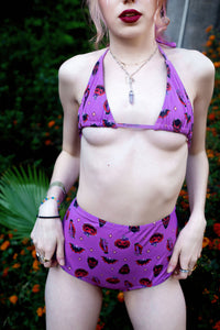 purple halter thin strap bikini top and high waist bikini bottom. Features black and orange images of pumpkins, bats, devil and hand holding cross