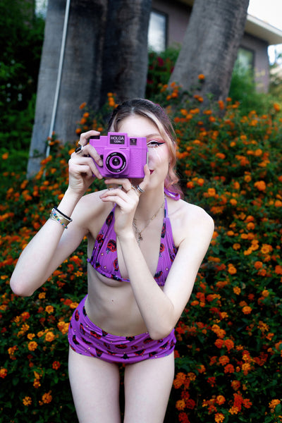 purple halter thin strap bikini top and high waist bikini bottom. Features black and orange images of pumpkins, bats, devil and hand holding cross