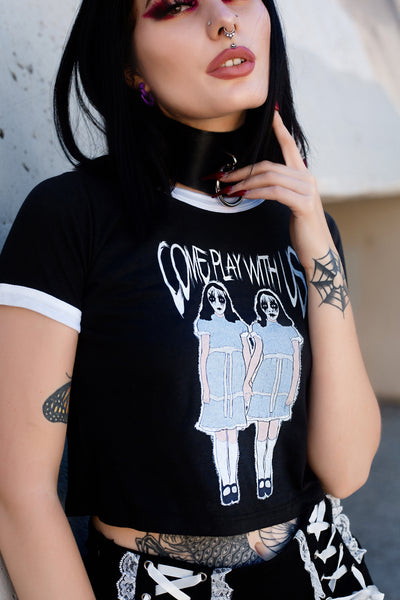 Black ringer tee with white trim. Features image of two girls holding hands with white and black face makeup wearing identical baby blue and white dresses with black shoes and white knee high stockings. Inscription reads "COME PLAY WITH US" in white.