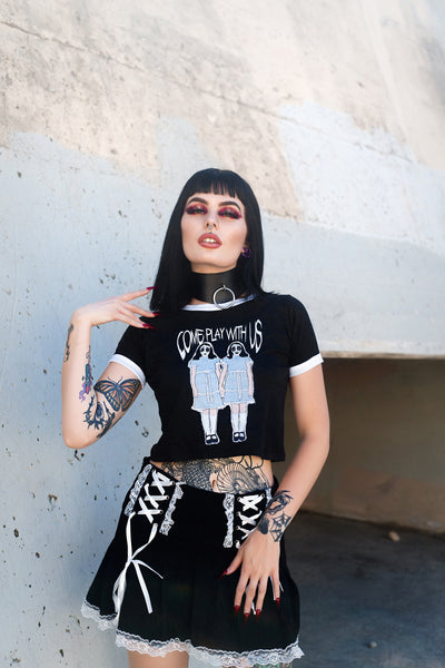 Black ringer tee with white trim. Features image of two girls holding hands with white and black face makeup wearing identical baby blue and white dresses with black shoes and white knee high stockings. Inscription reads "COME PLAY WITH US" in white.