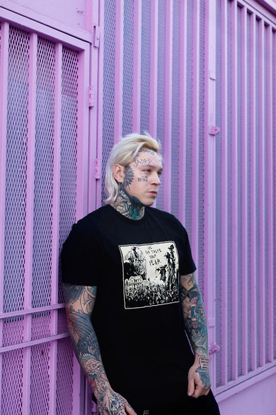 Black short sleeve t-shirt. Features black and white image of creeper from movie Jeepers Creepers face over house and cornfield with scarecrows and crows. Inscription reads "HE CAN TASTE YOUR FEAR" in black.