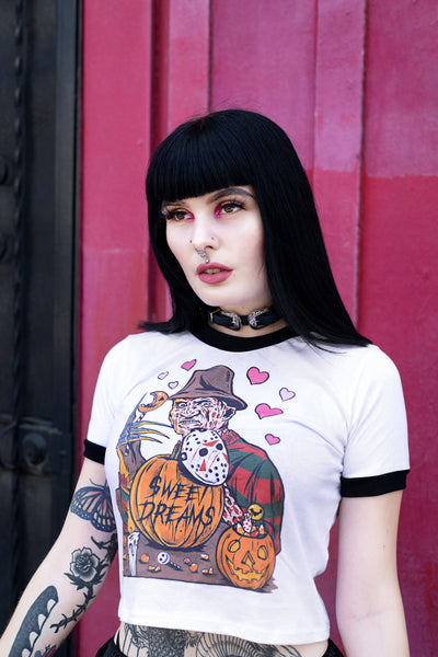 White ringer tee with black trim. Print is Freddy Krueger eating lollipop and has pumpkins and candy in front of him. On the pumpkins is a Jason hockey mask and pink hearts are behind Freddy. Center pumpkin says "Sweet Dreams" in black font