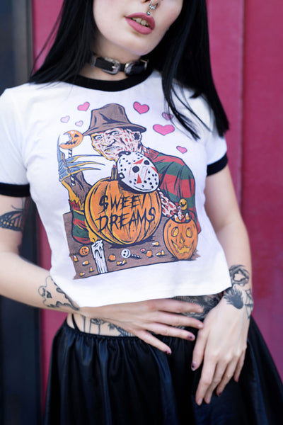 White ringer tee with black trim. Print is Freddy Krueger eating lollipop and has pumpkins and candy in front of him. On the pumpkins is a Jason hockey mask and pink hearts are behind Freddy. Center pumpkin says "Sweet Dreams" in black font