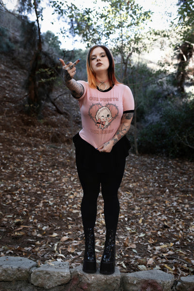 Baby pink ringer tee with black trim. Features image of a white cat wearing a pink bow winking inside a bob wire heart. Inscriptions reads "OUR PUSSY OUR CHOICE" in pink.