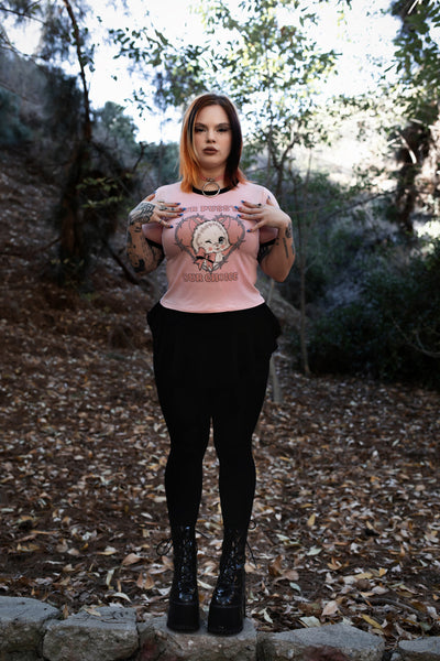 Baby pink ringer tee with black trim. Features image of a white cat wearing a pink bow winking inside a bob wire heart. Inscriptions reads "OUR PUSSY OUR CHOICE" in pink.