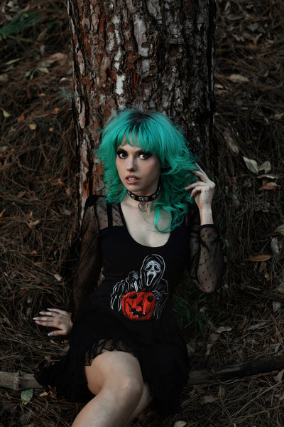 Black ballerina style dress with long sheer sleeves and sheer trim skirt. Print shows Ghostface from the movie Scream with knife and and orange Jack O lantern.