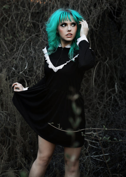 Black long sleeve, high neck, Victorian style dress with white lace trim neckline, cuffs and V shape trim from chest to shoulders. Black zipper down chest from neckline to V lace trim. Dress cinched at waist.