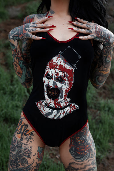 Black body suit with thin red trim neckline and thin red straps to tie around neck. Features clown from the movie Terrifier wearing a black top hat with red blood splattered on face.