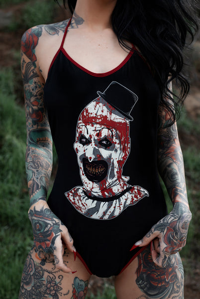 Black body suit with thin red trim neckline and thin red straps to tie around neck. Features clown from the movie Terrifier wearing a black top hat with red blood splattered on face.