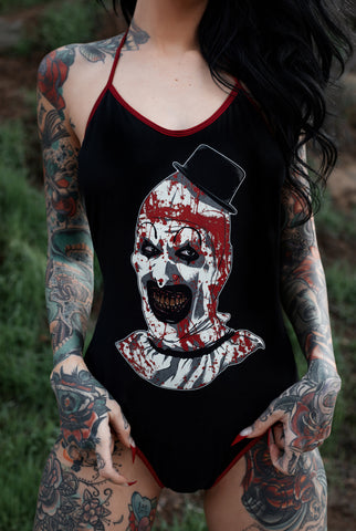 Black body suit with thin red trim neckline and thin red straps to tie around neck. Features clown from the movie Terrifier wearing a black top hat with red blood splattered on face.