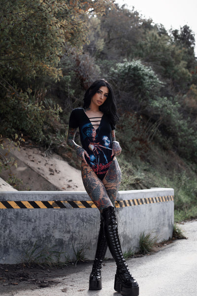 Black short sleeve bodysuit with black lace up V neck. Features Freddy Krueger holding knife glove up to woman's face with houses below. Inscription reads "A Nightmare on Elm Street" in red.