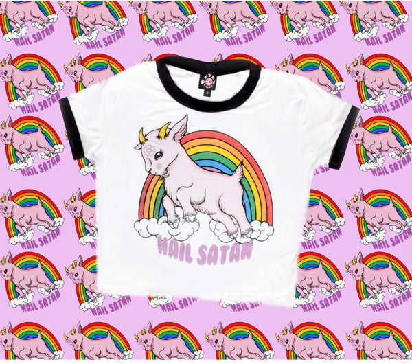 White ringer tee with black trim. Features animated pink goat with pentagram on forehead. Clouds and rainbow behind goat. Written underneath goat is "Hail Satan" in pink font.