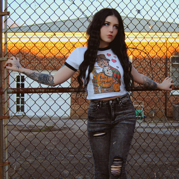 White ringer tee with black trim. Print is Freddy Krueger eating lollipop and has pumpkins and candy in front of him. On the pumpkins is a Jason hockey mask and pink hearts are behind Freddy. Center pumpkin says "Sweet Dreams" in black font