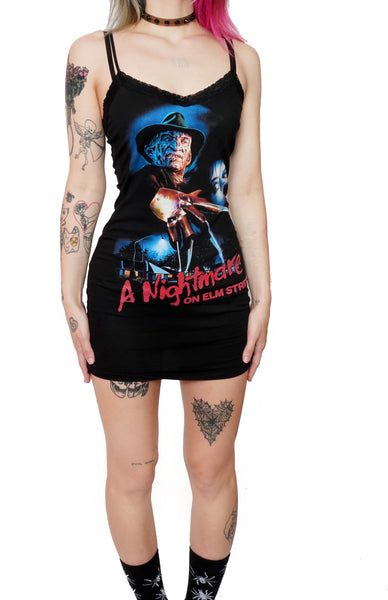 black mini dress with thin straps and lace trim neckline. Features Freddy Krueger with scared female. Beneath Freddy there are houses and a street light. Inscription reads "A Nightmare on Elm Street" in red.