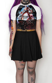 Solid black baby doll style dress with white baseball short sleeves and white trim neckline. Features image of man carrying a chainsaw with woman to her knees holding his leg. Battle and castle appear in the background. Inscription reads "Army of Darkness" in yellow.