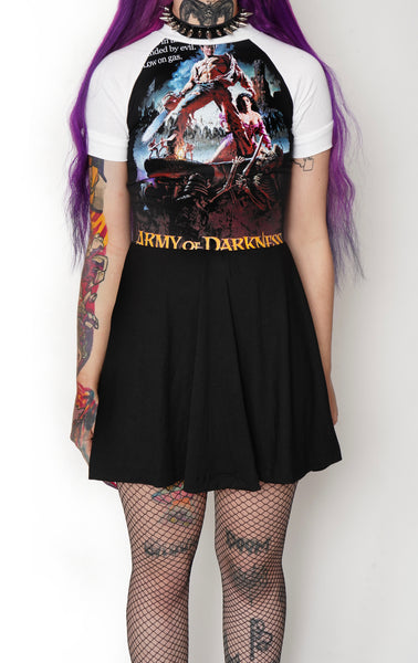 Solid black baby doll style dress with white baseball short sleeves and white trim neckline. Features image of man carrying a chainsaw with woman to her knees holding his leg. Battle and castle appear in the background. Inscription reads "Army of Darkness" in yellow.