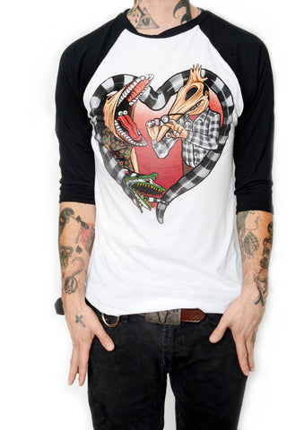 White baseball tee with black sleeves and black neckline trim. Features image of Barbara and Adam from the movie Beetlejuice. Barbara has face stretched with mouth open, tongue sticking out and eyes in mouth. Adam has his face stretched out with eyeballs on his fingers and glasses in hand. Black and white Beetlejuice snake around Adam and Barbara in the shape of a heart.